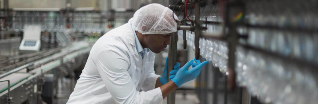 Plastics worker in a lab coat inspecting an assembly line of plastic material within a factory setting.