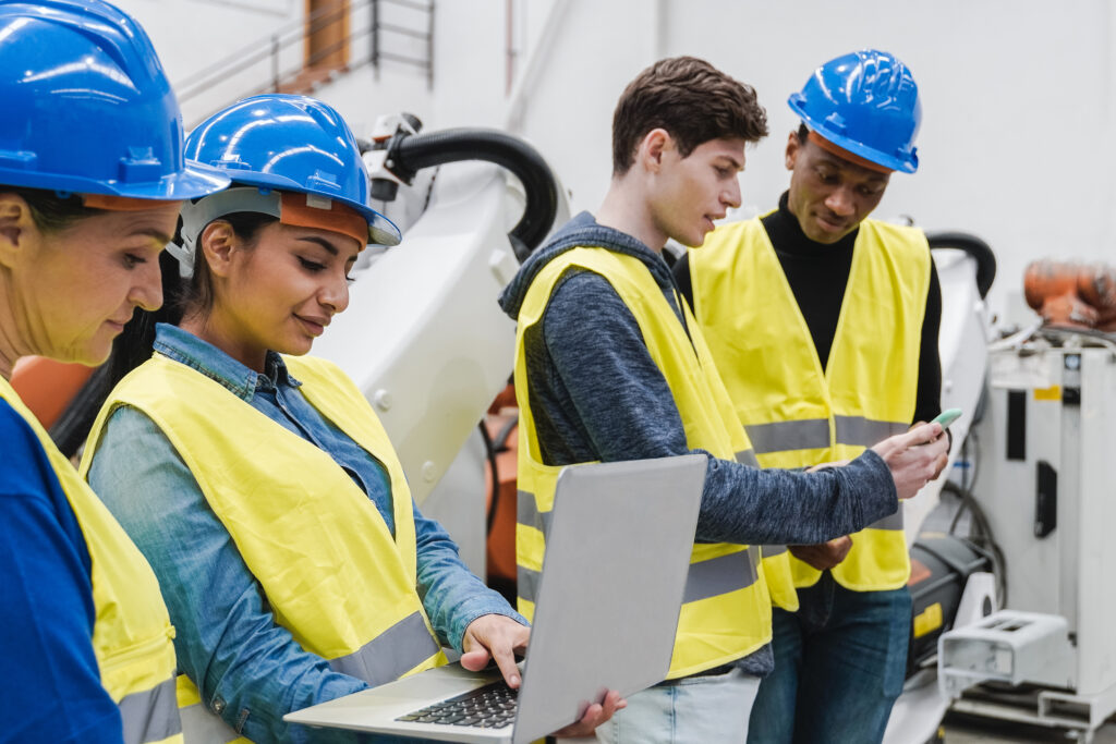 Industrial plastic manufacturing engineers working inside of a factory reviewing numbers on laptops and product assessment