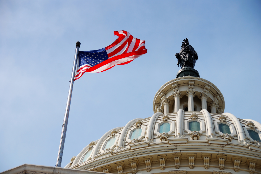 A close-up of the US government office and an American flag waving in the wind to represent US Government Roles in the Plastics Industry