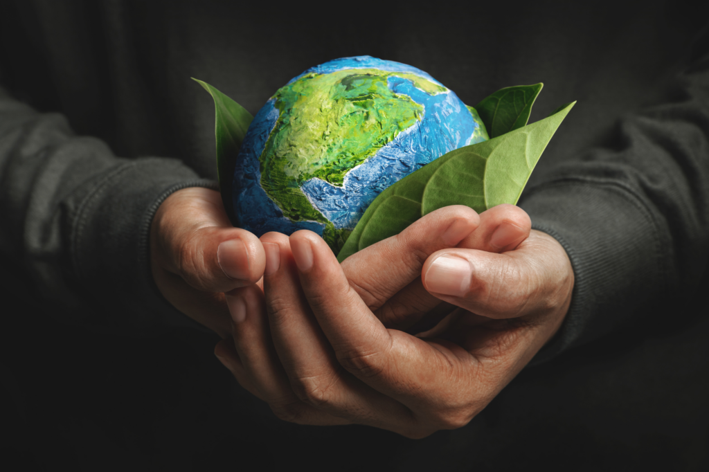A close-up of a man's hands tenderly holding Earth with some green leaves surrounding it. This photo symbolizes the future of plastics and how The New Plastics Economy way of thinking is shifted toward a more sustainable approach.
