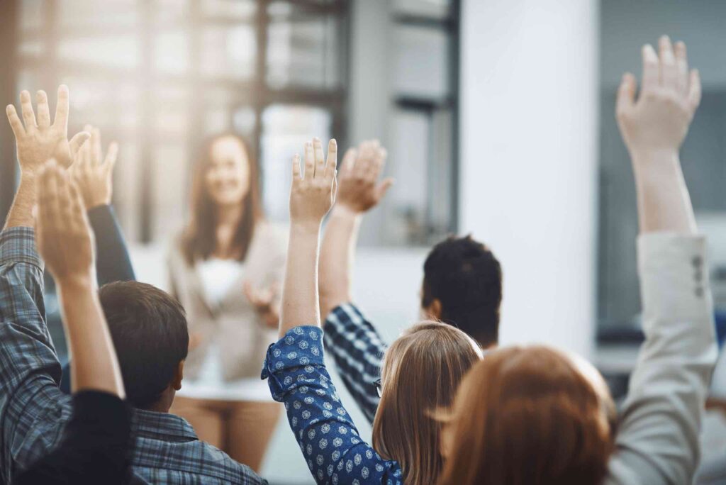 A plastics recruiter standing at the front of a conference room in front of several plastics candidates with their hands raised. This represents the common questions candidates ask plastics recruiters during the recruitment process.