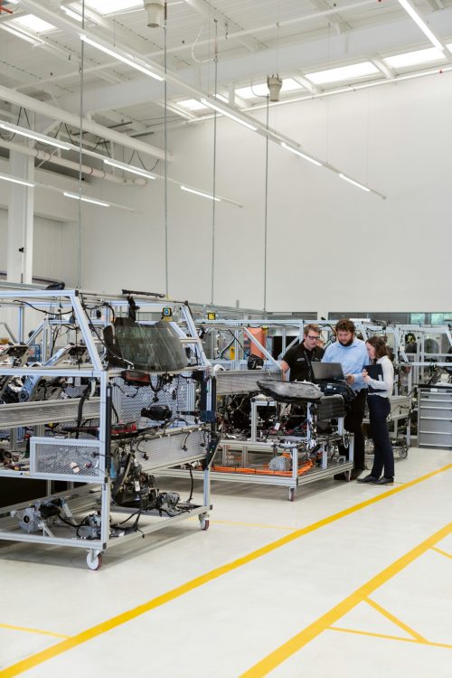 Three workers hovering over a computer in a factory setting with plenty of technology around them.